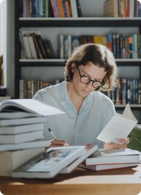 Студент в очках учится за столом, обложившись книгами